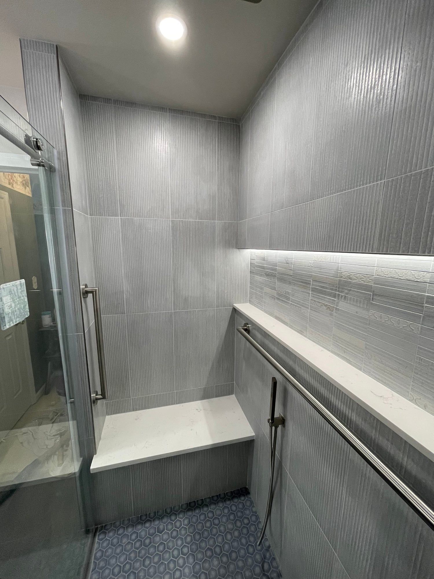 Tiled shower bench with quartz top under a lit niche