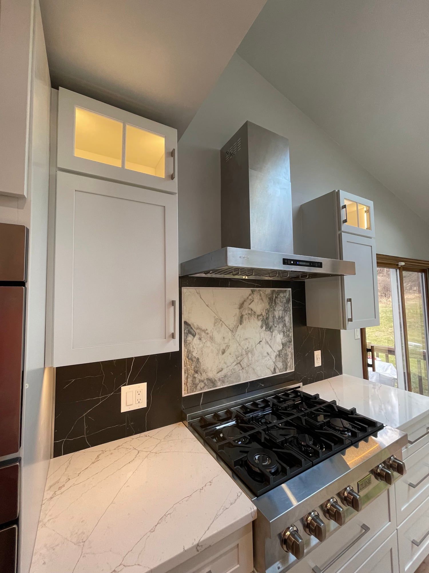 Stone slab backsplash framed by black tile under a chimney hood