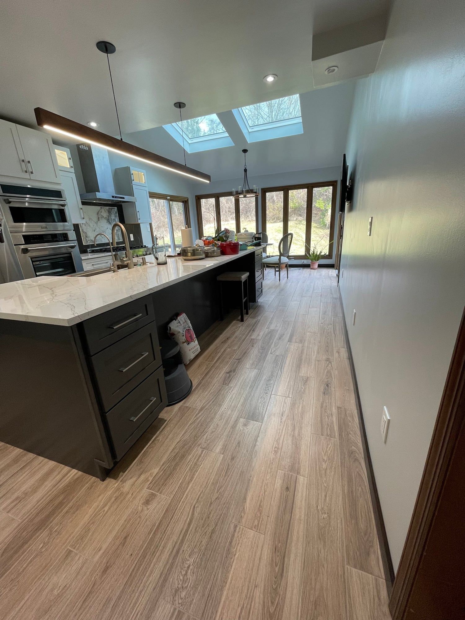 Long dark island with quartz top under a linear pendant, skylights and a wall of windows beyond