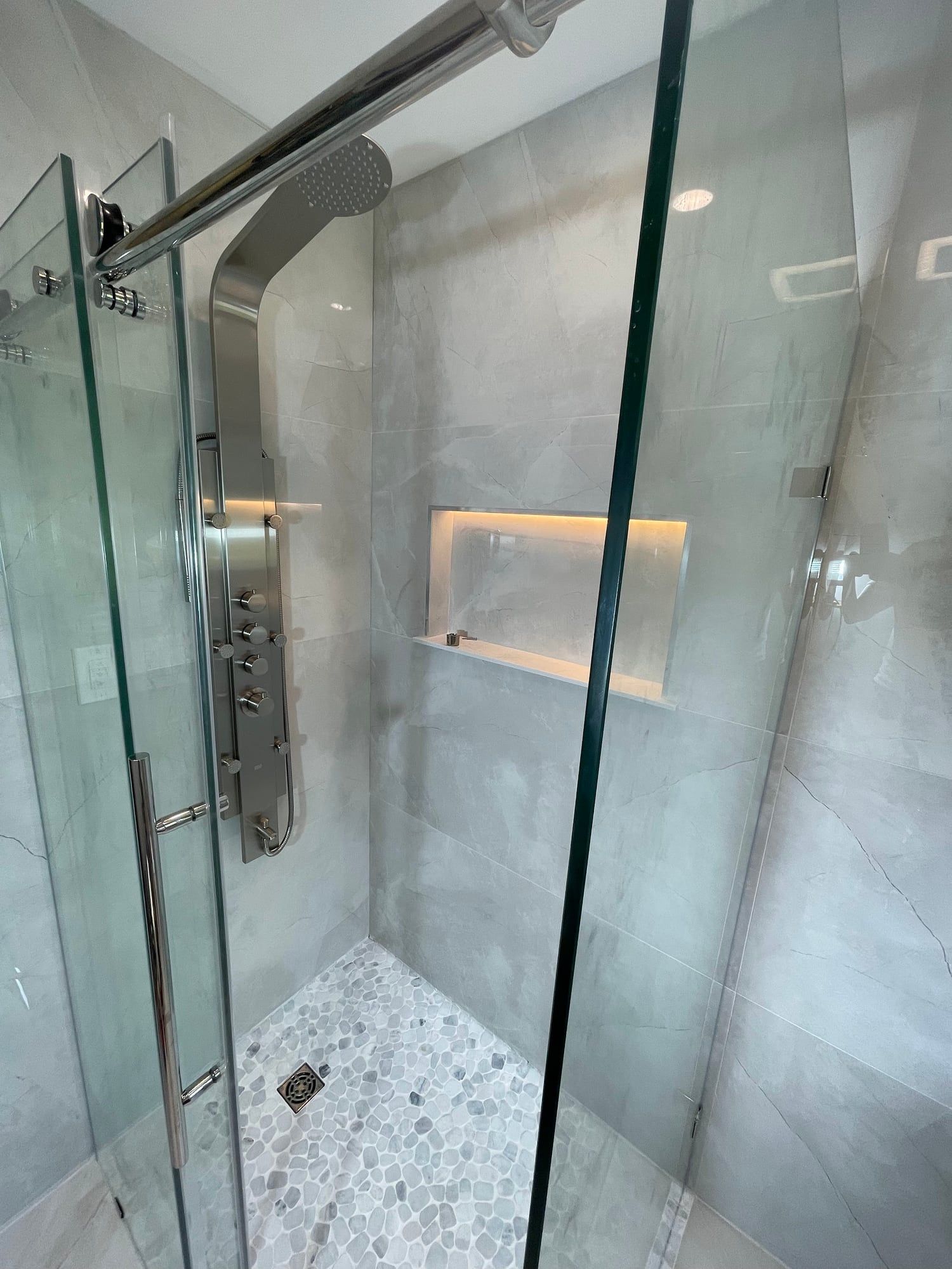 Shower with a stainless shower panel, lit niche and pebble floor