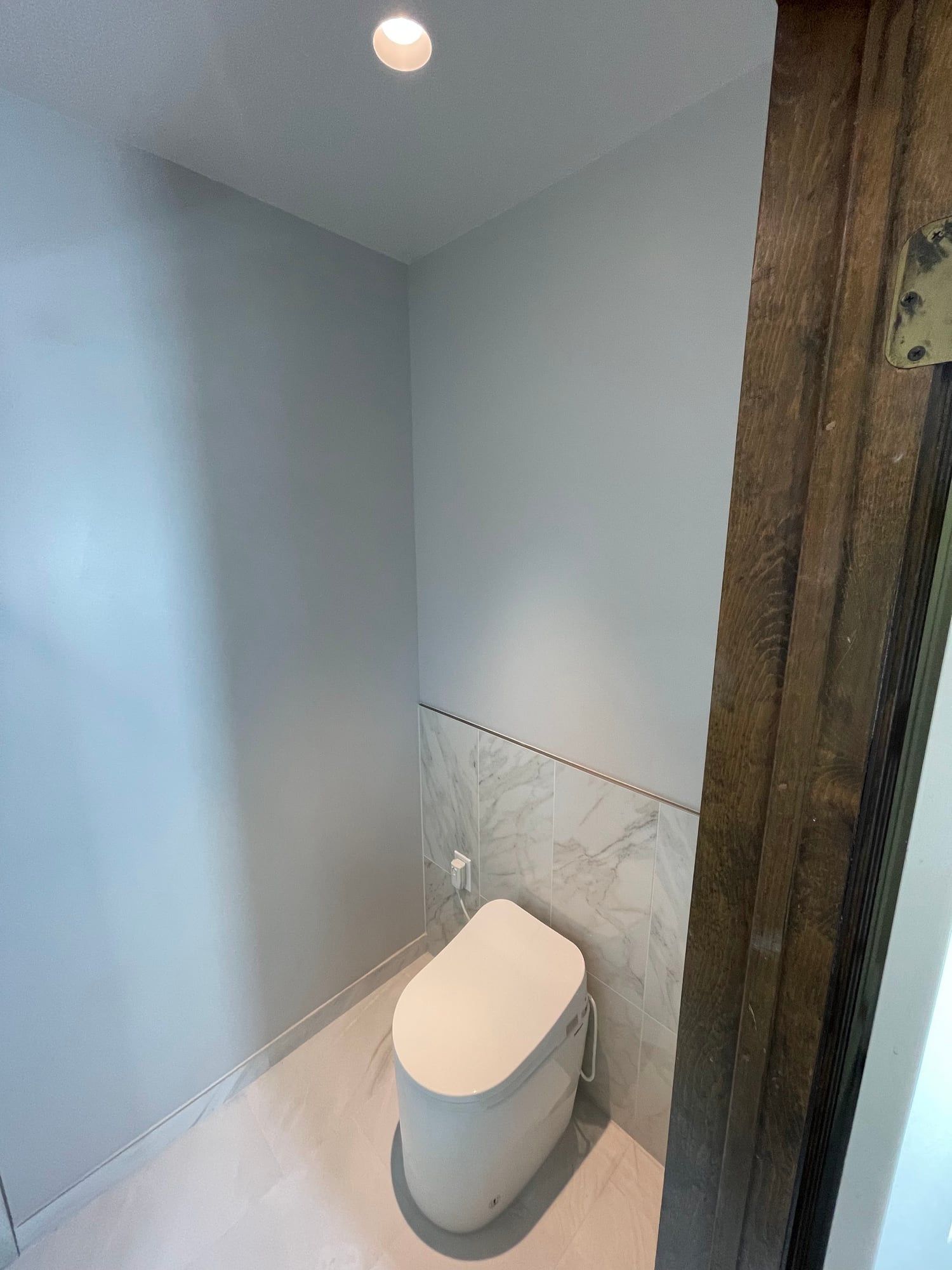 Powder room with a compact toilet and marble-look wainscot
