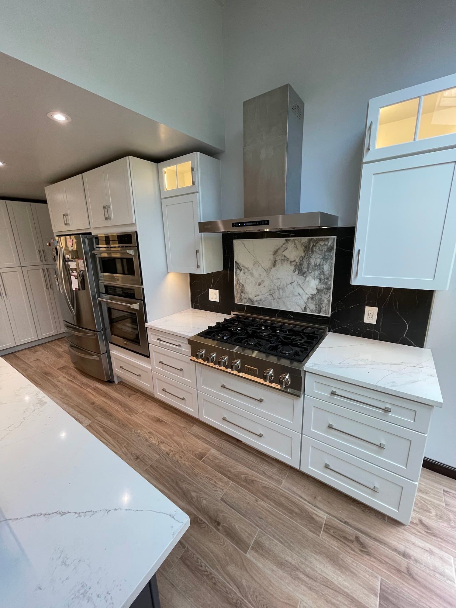 After: white shaker cabinetry, stacked wall ovens and a range under a chimney hood