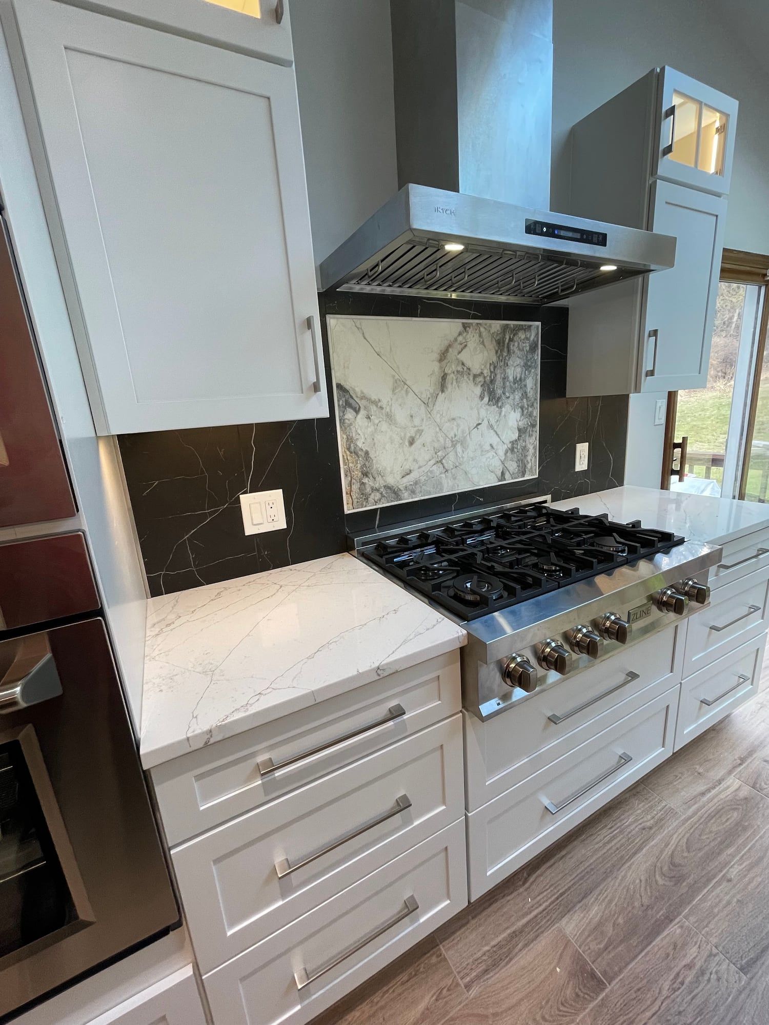 Pro-style gas range under a stainless hood with a stone slab backsplash