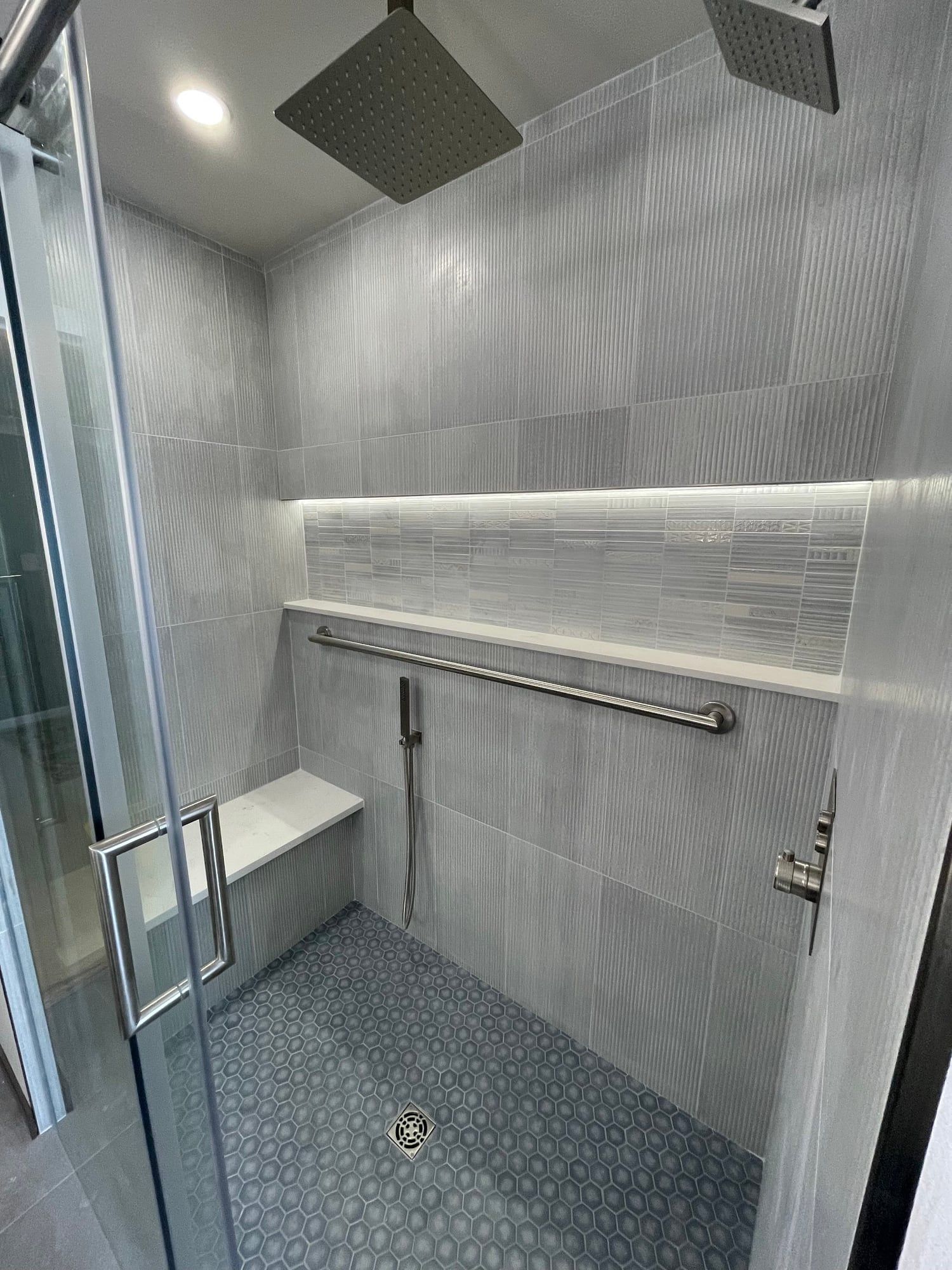 Walk-in shower with a tiled bench, rain heads and a lit niche