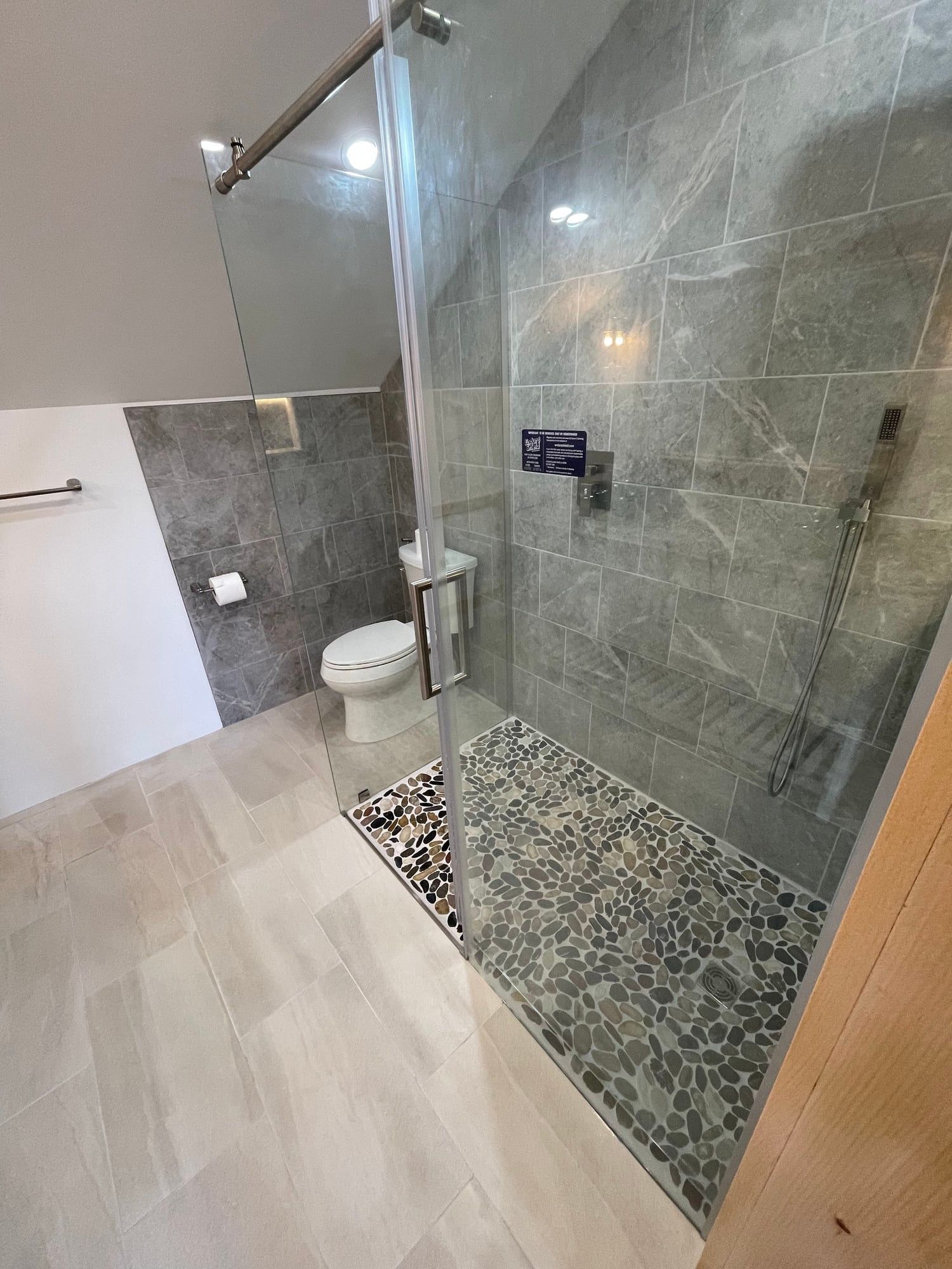 Frameless glass shower with gray tile and a pebble floor