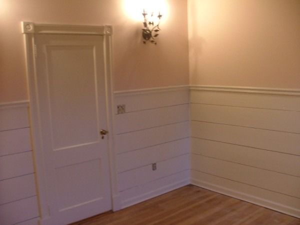 Room with white plank wainscot, a paneled door and wall sconces