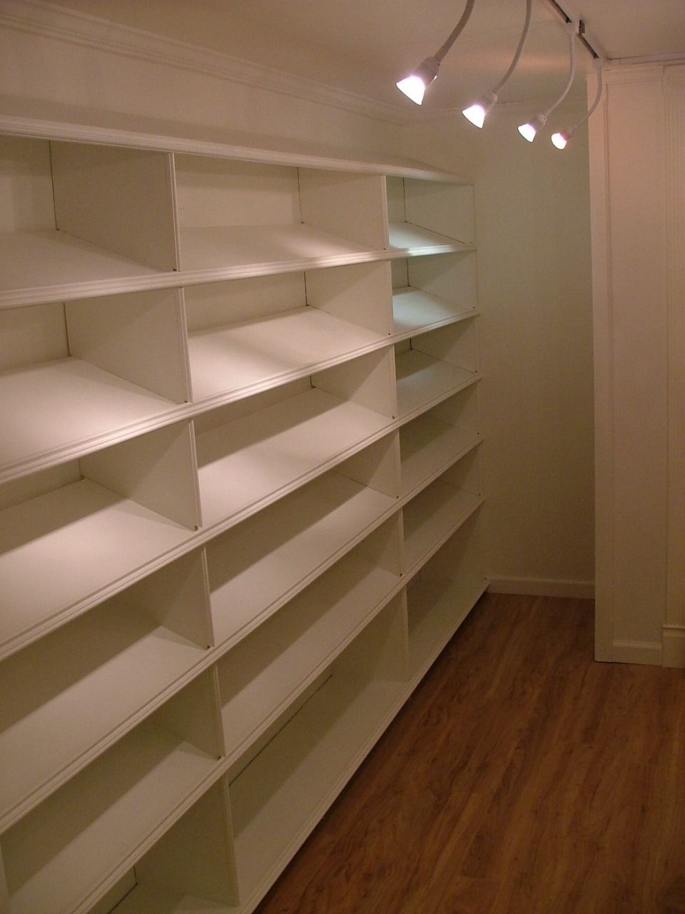 Floor-to-ceiling white shelving lit by track lights