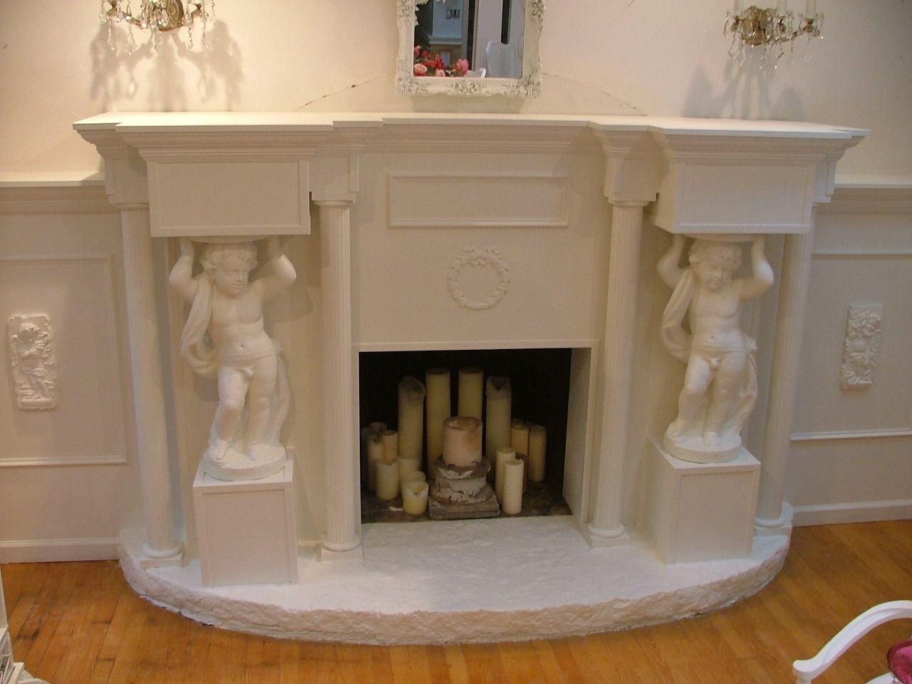 White fireplace surround with pilasters, carved panels and two sculpted figures, candles in the firebox