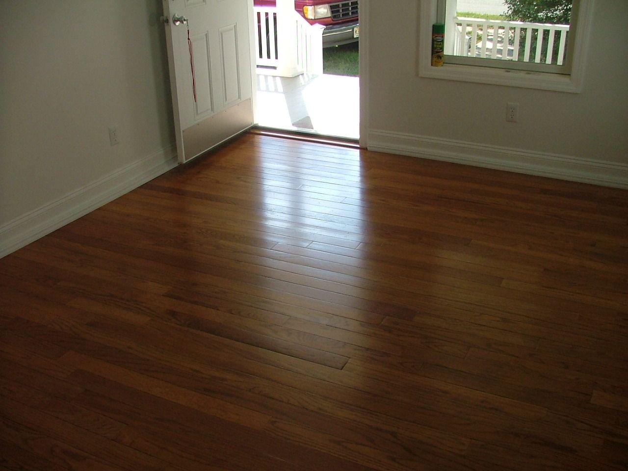 Finished hardwood floor in an empty room with white trim